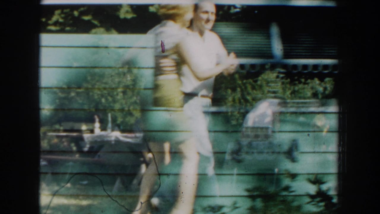 In 1959 Michigan home-movie footage, a young couple dances outdoors beside a green-sided house with trees and patio items nearby.
