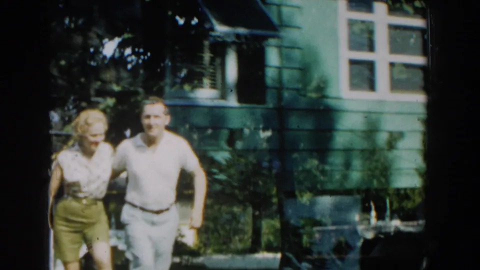 The couple faces the camera together in the Michigan yard, framed by green siding, windows, foliage, and soft 8mm color shifts.