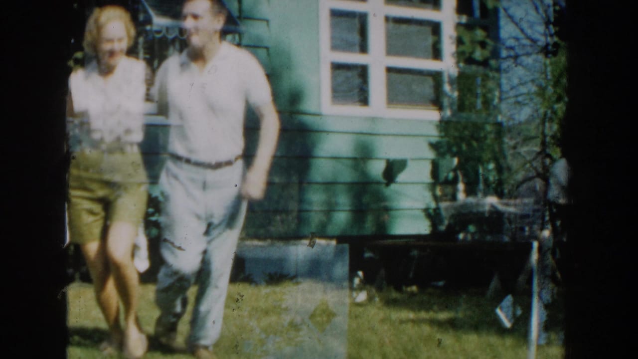 Young couple walking beside a green-sided house in a sunny yard.