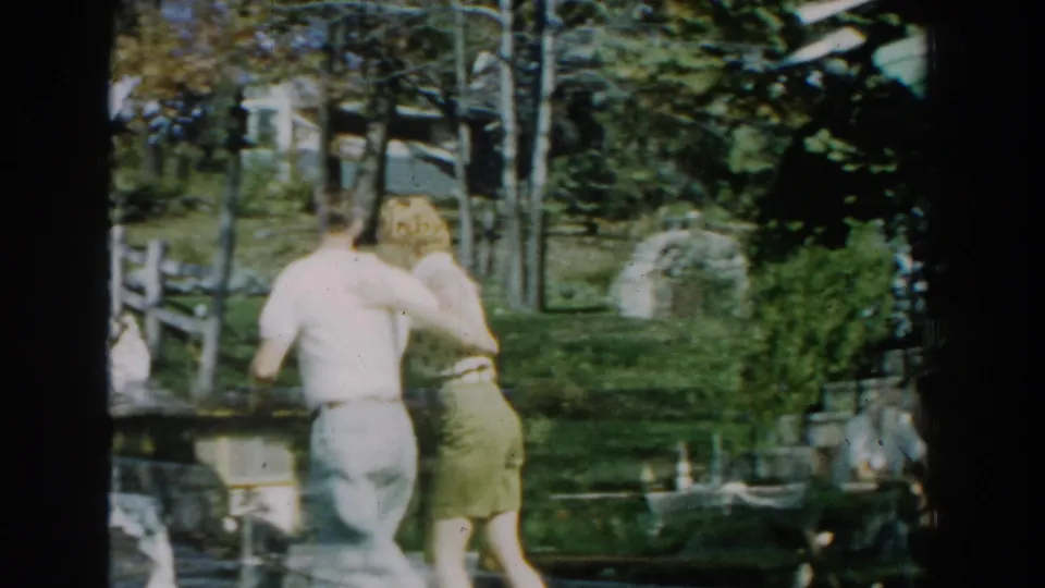 Seen from behind, the couple walks arm-in-arm through the Michigan backyard toward trees and fencing.