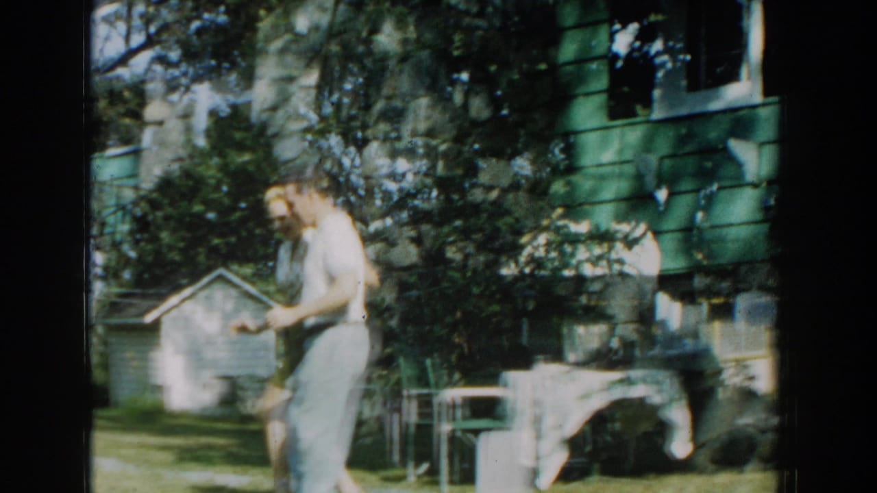 A couple dances close together in a backyard near lawn chairs, shrubs, and a house.