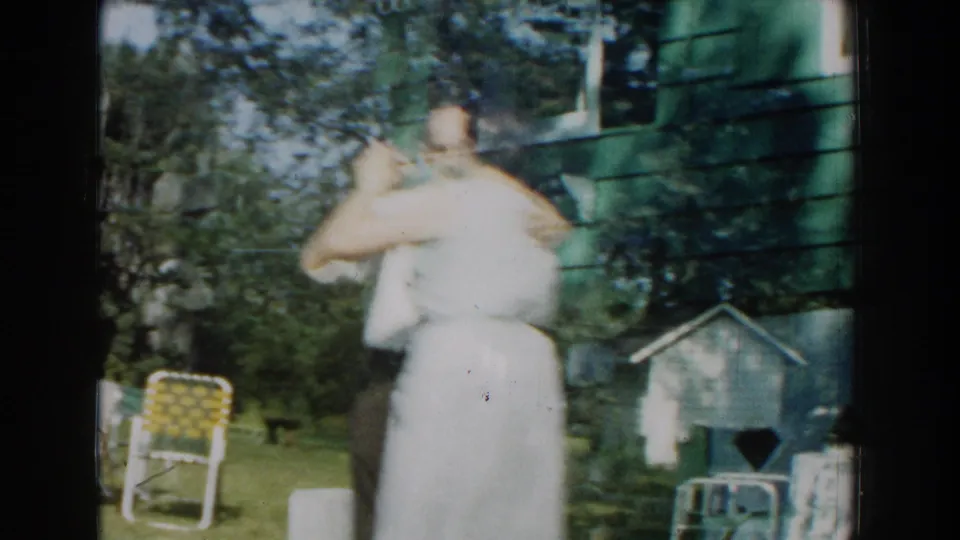 The couple dances in close hold on a lawn, with mid-century outdoor chairs and a small backyard structure visible nearby.
