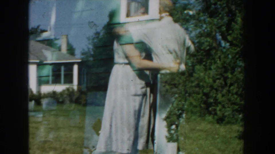 A woman in a light dress dances near the side of a Michigan house, with her partner partly hidden by motion and framing.