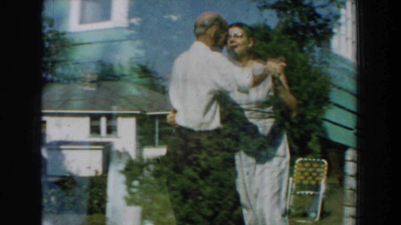Elderly couple dancing beside a house in a sunny backyard.