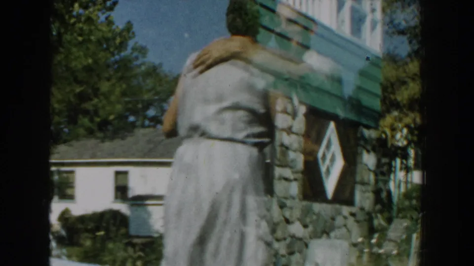 The couple turns with their arms around each other beside a house with stone siding in the Michigan backyard scene.