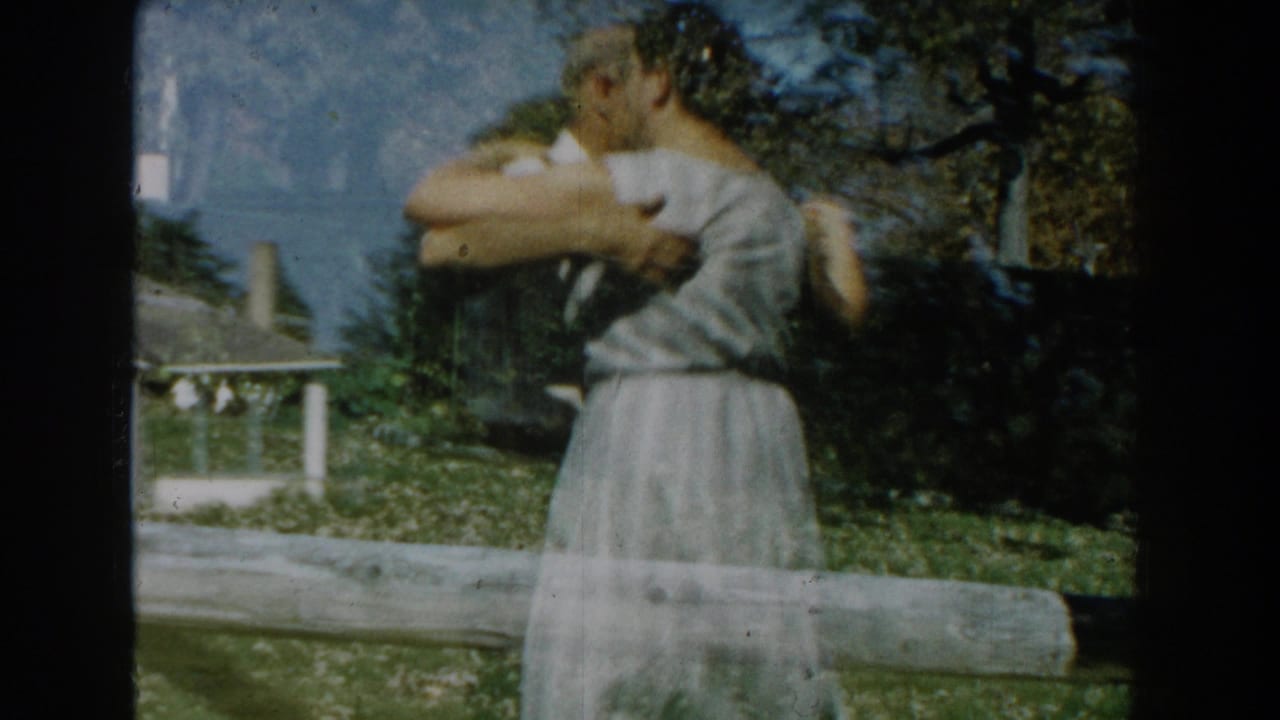 Couple dancing closely on a sunny lawn near a low rail and house.