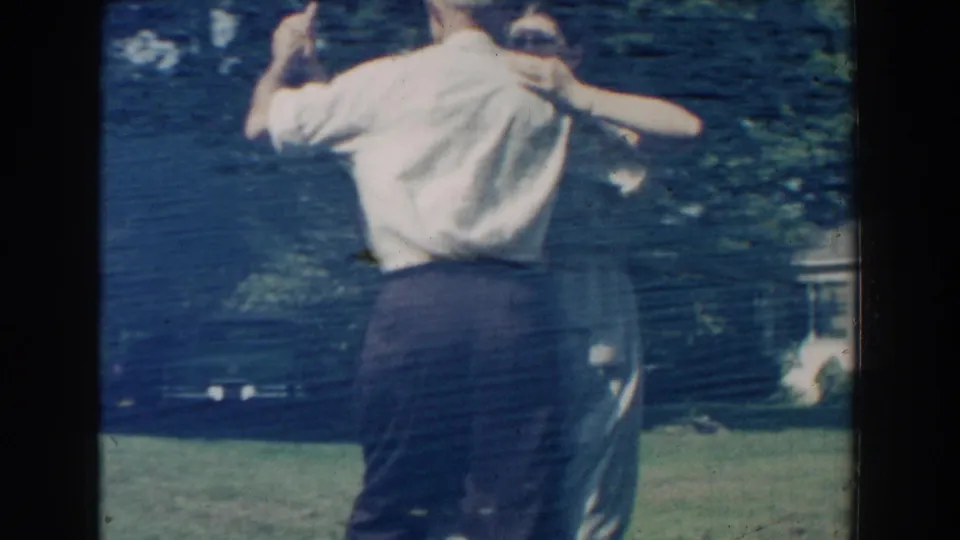 From behind, the man and woman continue dancing on the Michigan lawn, framed by trees and a modest house exterior.