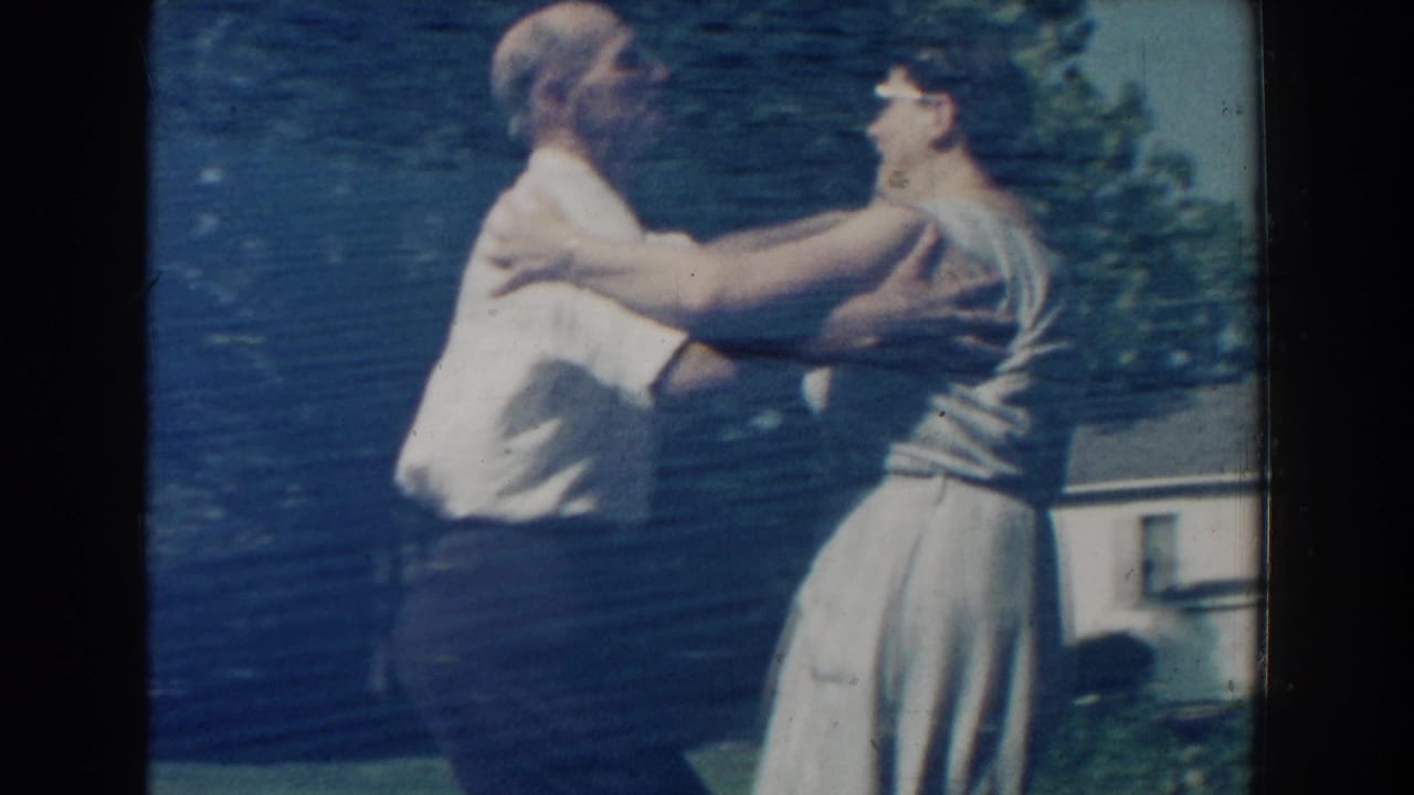 In this 1959 Michigan home-movie frame, an older couple holds each other while dancing in a suburban backyard.