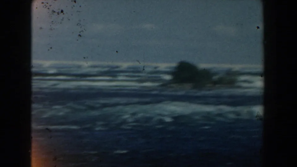 1959 Michigan 8mm frame showing dark blue waves, a low tree-covered shore, pale horizon, and dust marks on the film.