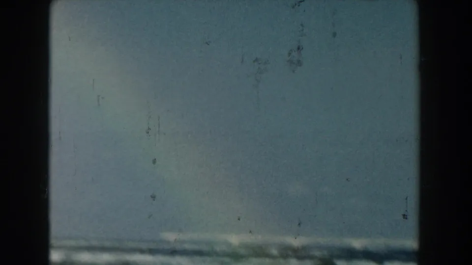 1959 Michigan 8mm frame with a low horizon of waves beneath open blue sky, marked by light scratches and home-movie grain.