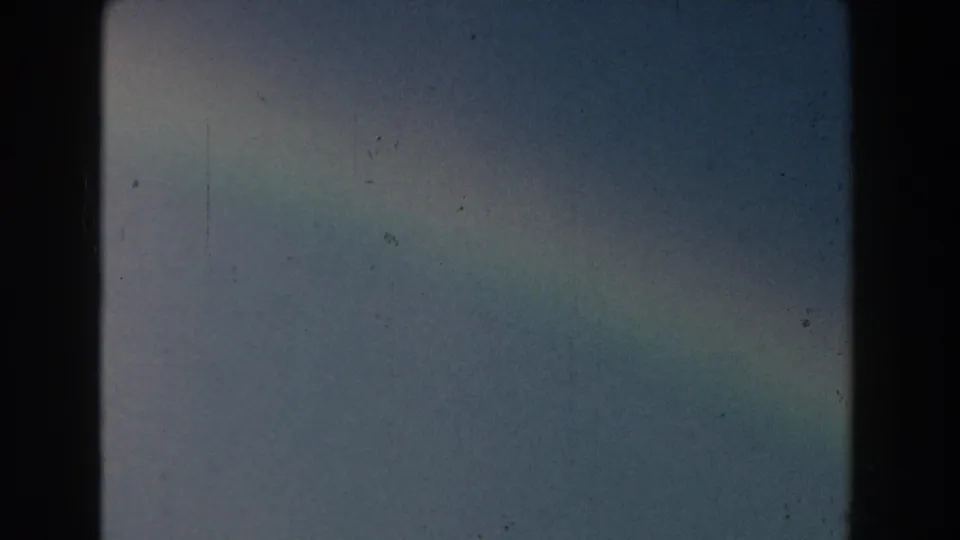 1959 Michigan 8mm frame showing a soft rainbow arc across pale sky, with grain, dust, and color fading visible.