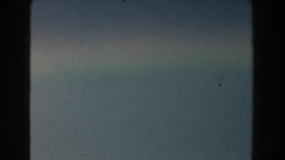 1959 Michigan 8mm frame with blue-gray sky, thin haze, subtle cloud texture, and dark film gate edges.