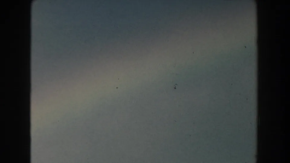 1959 Michigan 8mm frame showing muted hazy sky, pale cloud band, and faint rainbow color low in the frame.