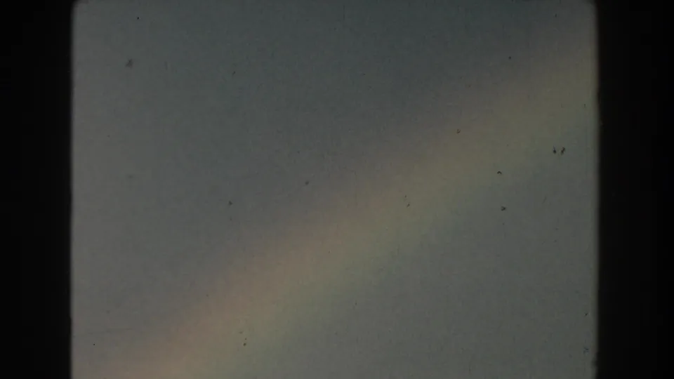 1959 Michigan 8mm frame with a faint rainbow arc against hazy blue-gray sky and visible scanned film edges.