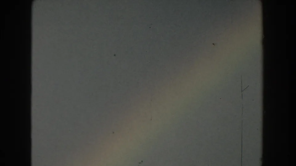Faint rainbow in a cloudy Michigan sky from 1959 8mm home-movie footage, framed by dark gate edges and visible film wear.