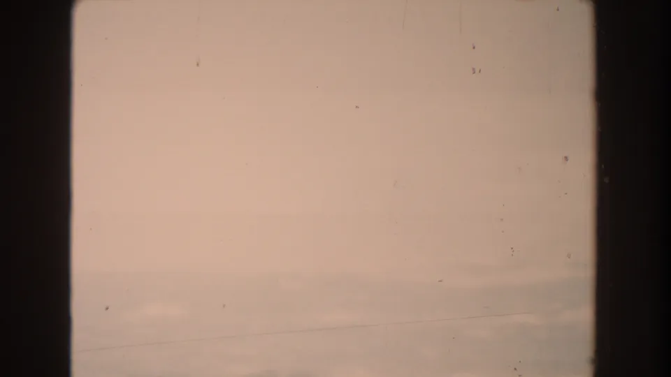 Soft pink post-rain sky in 1959 Michigan 8mm footage, with low cloud bands, dust specks, scratches, and dark frame edges.