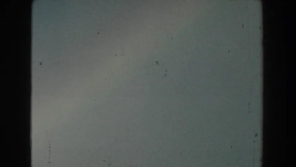 Soft 8mm frame from the Michigan clip showing mostly hazy sky, visible gate edges, and scattered film dust.