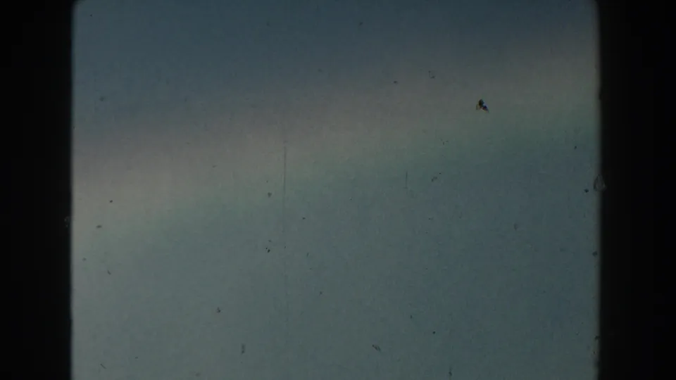 Hazy Michigan sky in 1959 8mm footage with a faint rainbow band and visible film-frame edges.
