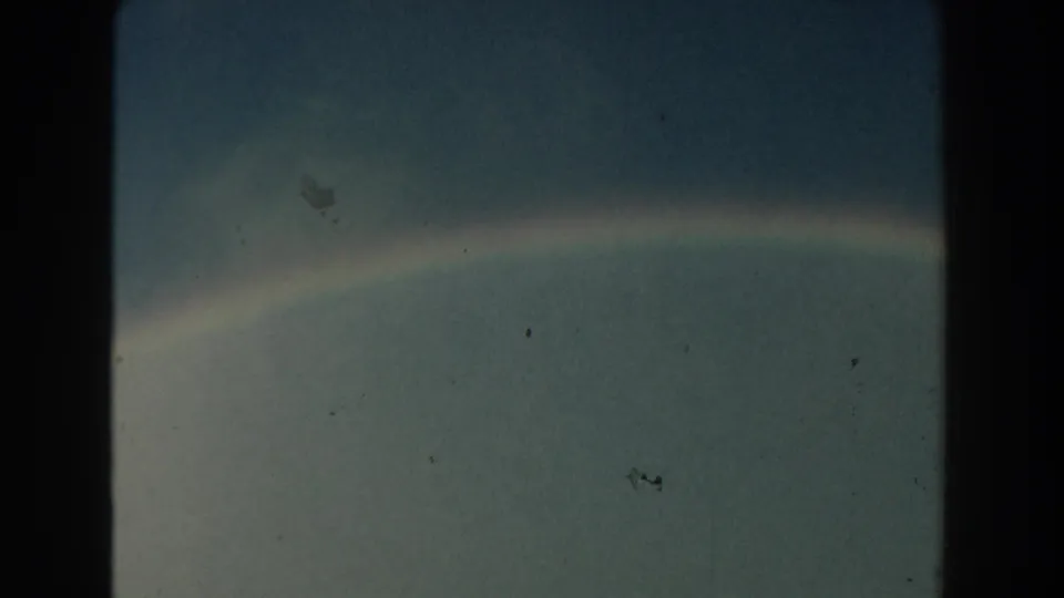 1959 Michigan 8mm frame with a soft rainbow band stretching through a subdued sky and aged-film texture.