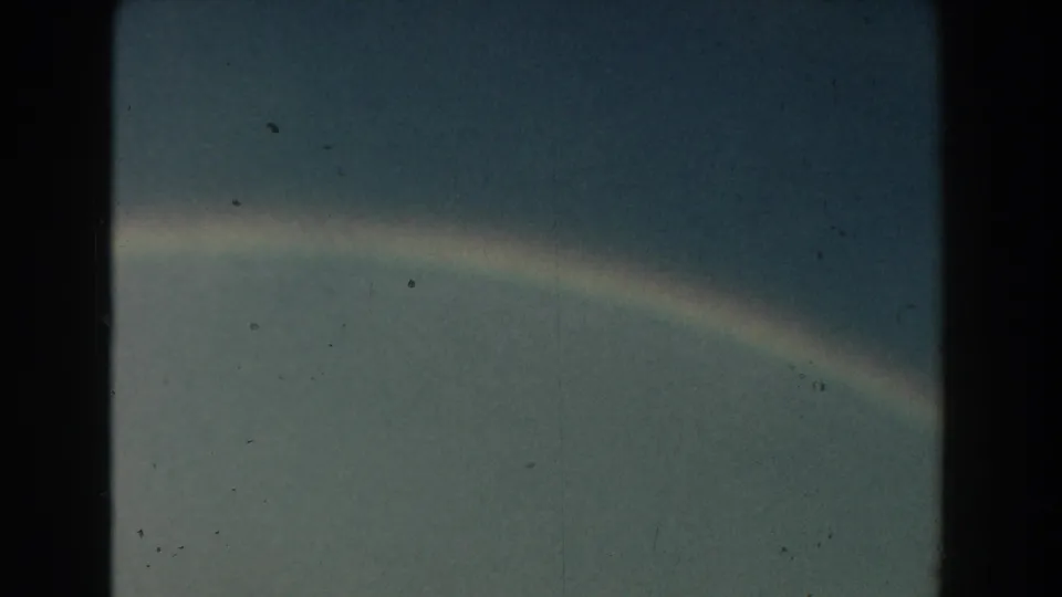 1959 Michigan 8mm frame showing the lower curve of a rainbow through haze, with grain and light wear visible.