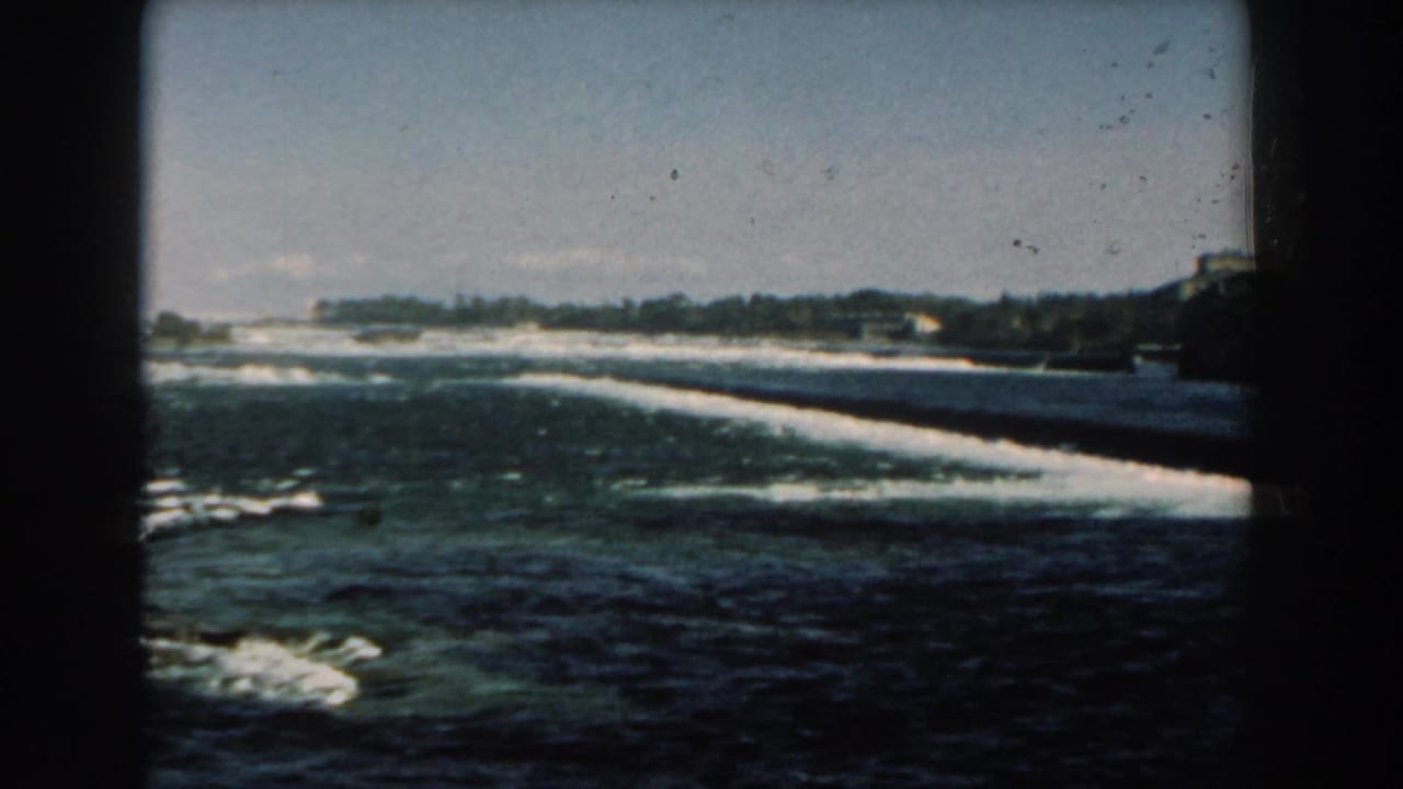 Shoreline with waves and distant buildings seen through dark film-frame edges.