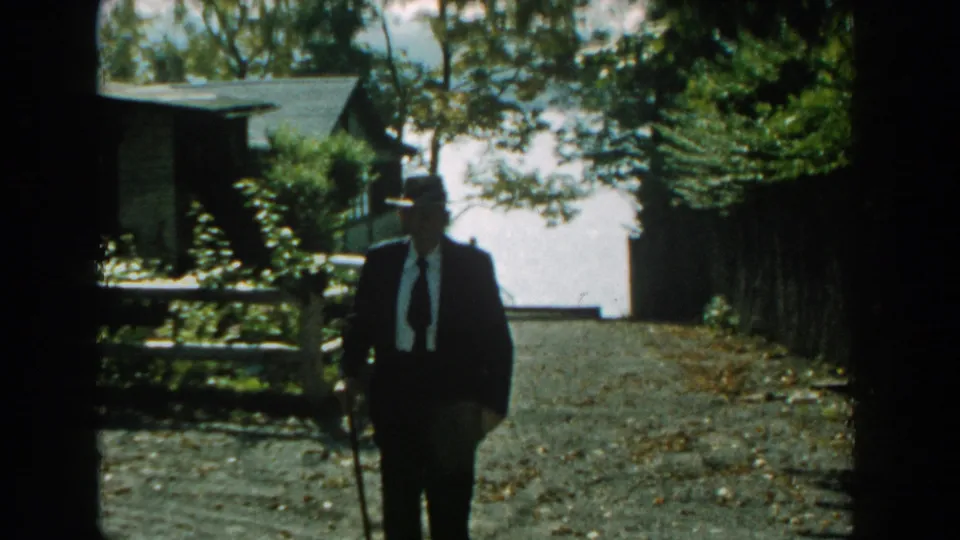 The man appears farther from the camera near a fence and house exterior in the closing 1959 Michigan 8mm frame.