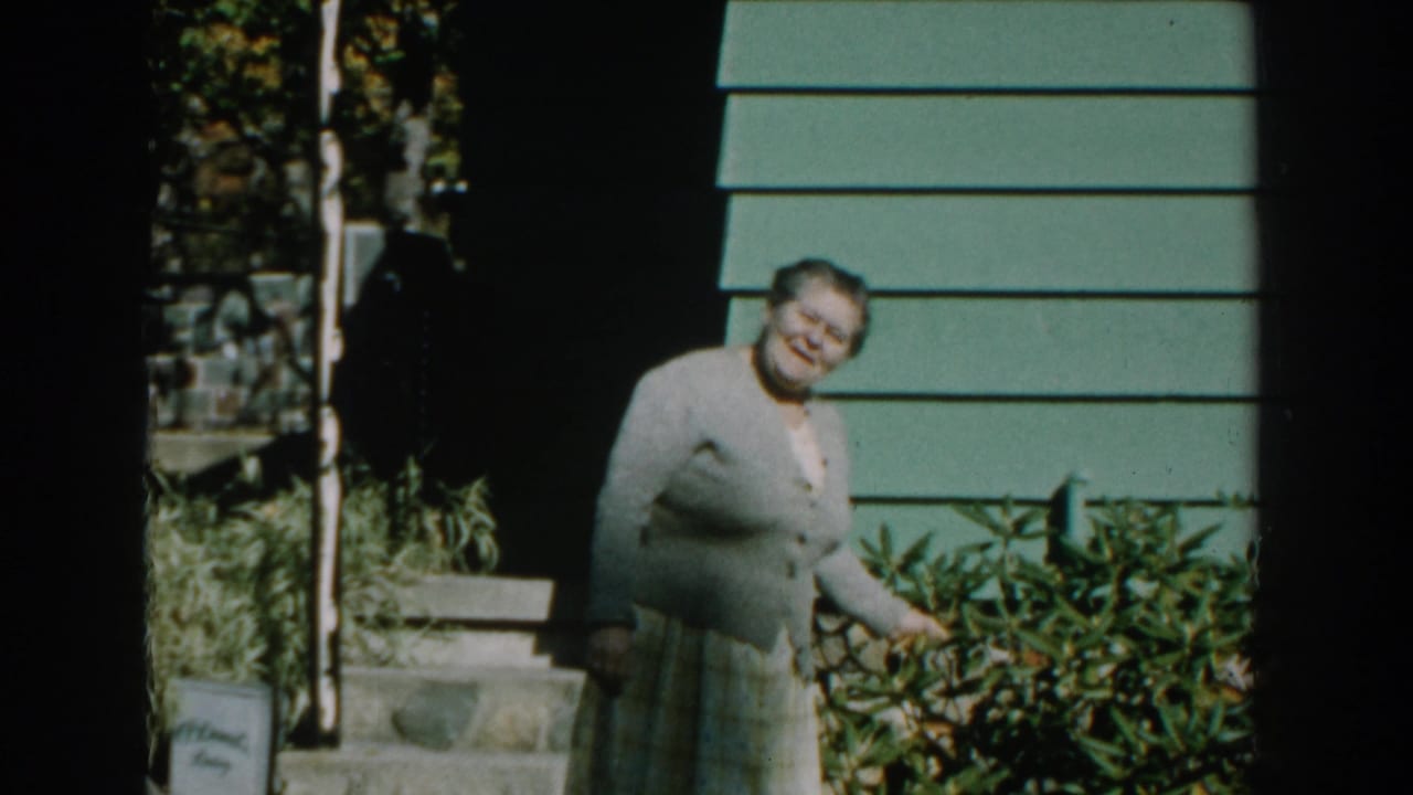 Woman turns from the shrubs and smiles toward the camera outside the house.