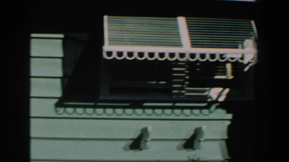 1959 Michigan home-movie frame showing green house siding, a window, and a striped scalloped awning in strong sunlight.
