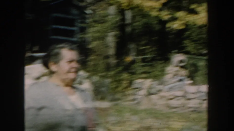 The handheld 8mm frame catches the woman in motion blur as she passes garden foliage and a low stone wall in Michigan.