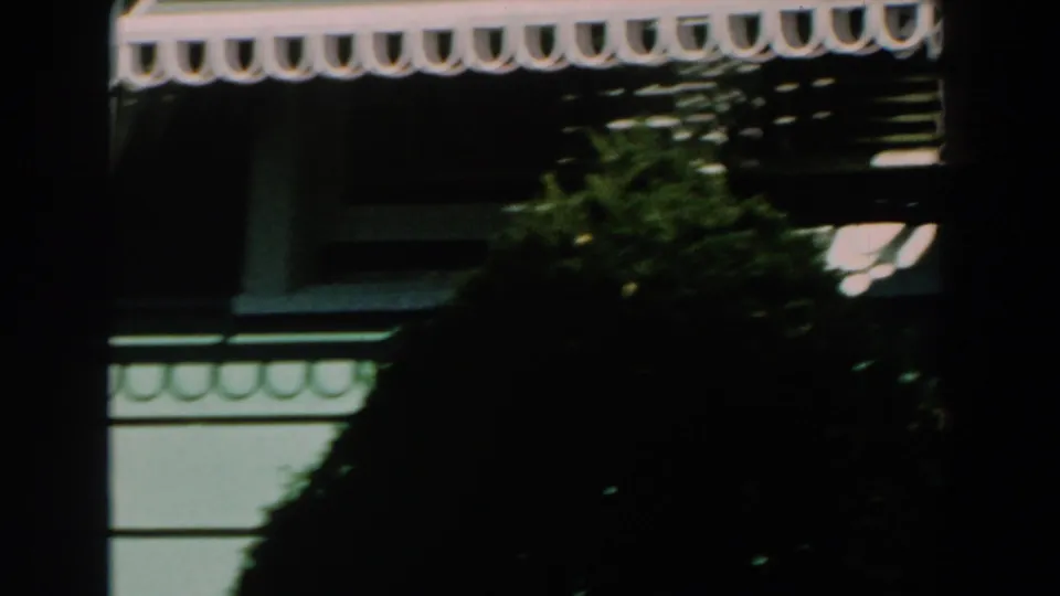 1959 Michigan frame showing a white scalloped awning, green house trim, shrubbery, and strong shadow across the exterior.
