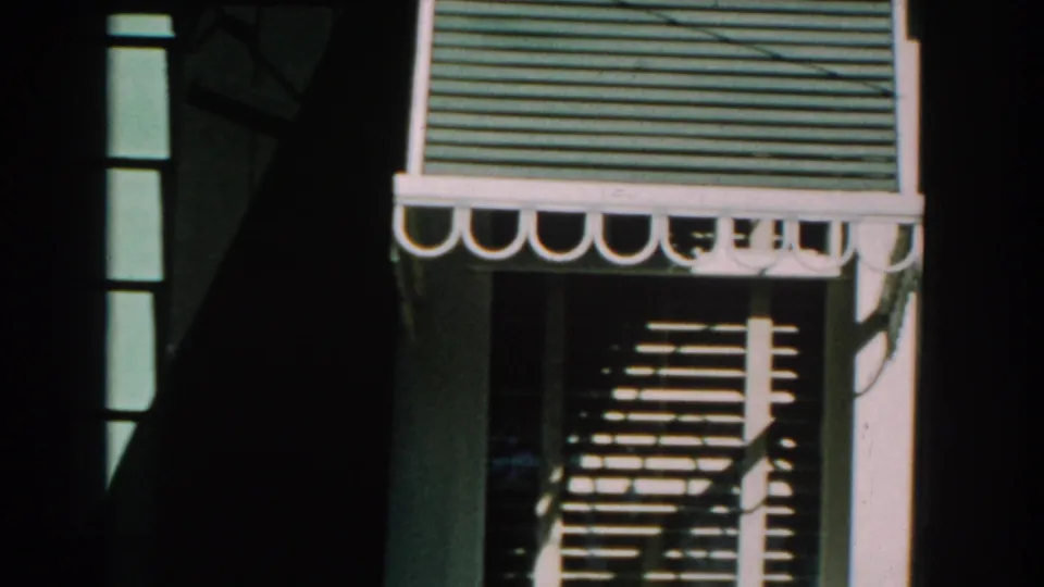 1959 Michigan home-movie frame showing a striped awning, window trim, and strong shadows on a bungalow wall.