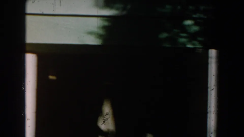 1959 Michigan 8mm frame showing the lower portion of a green house exterior, a shaded porch area, and a white support post.