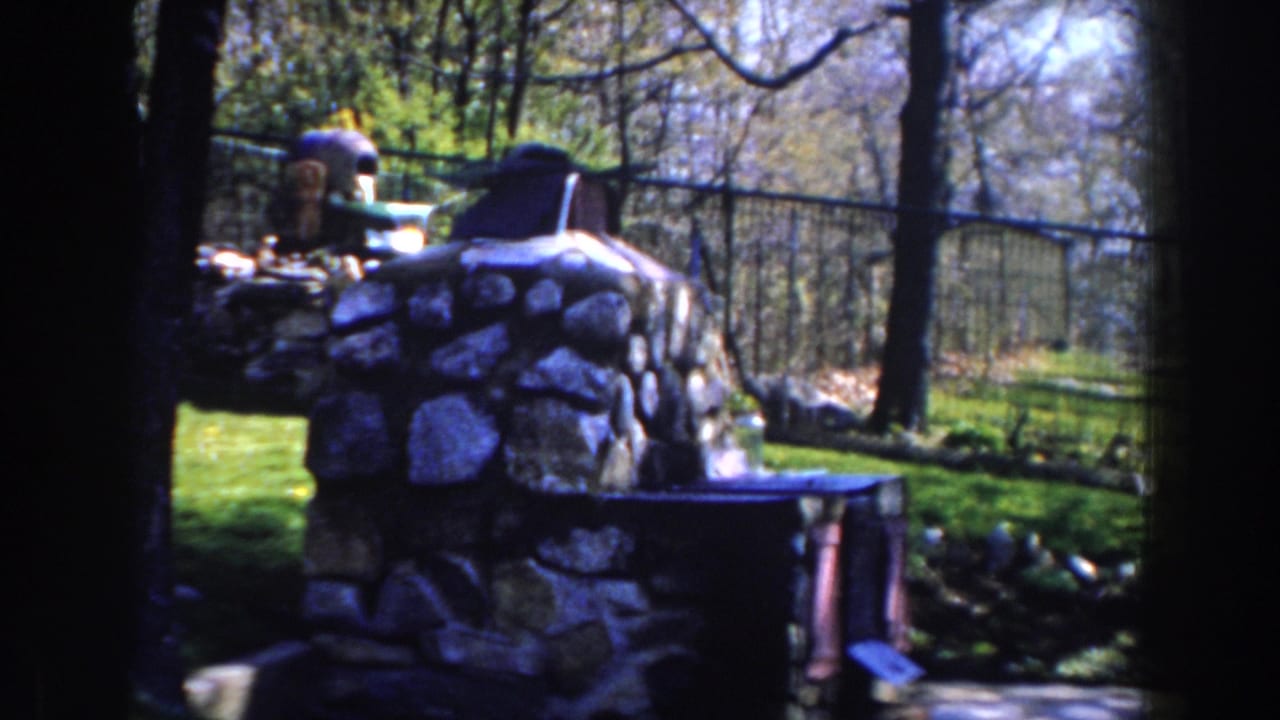 Stone fireplace and lawn framed by trees with a fence in the background.