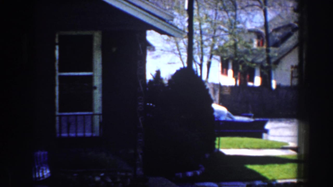 House exterior partly blocked by a dark vertical shape, with lawn and neighboring homes beyond.