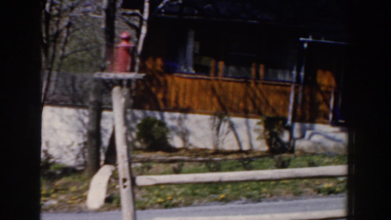 House exterior across a street with white fence rails, a red fire hydrant, lawn, and trees.