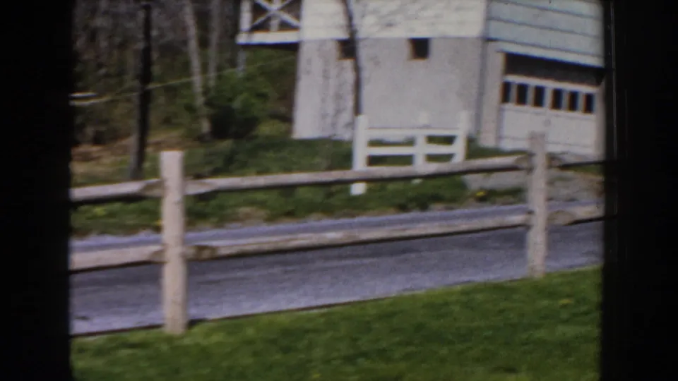 1959 Michigan suburban frame showing a garage, driveway, white fence sections, lawn, trees, and the road in front.