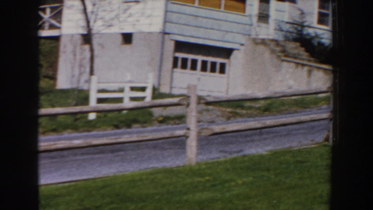 Suburban house with garage, split-rail fence, road, and front lawn.