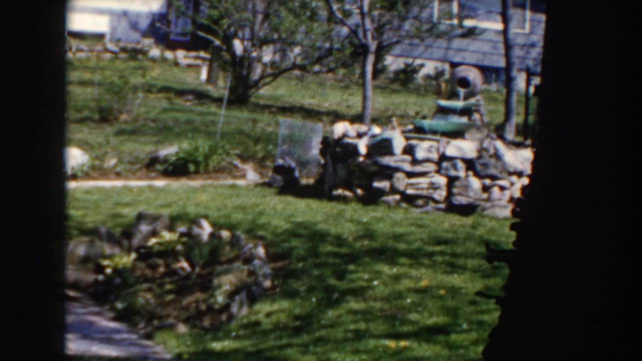 1959 Michigan backyard view centered on a tiered green fountain set into a low stone wall, with lawn and trees around it.