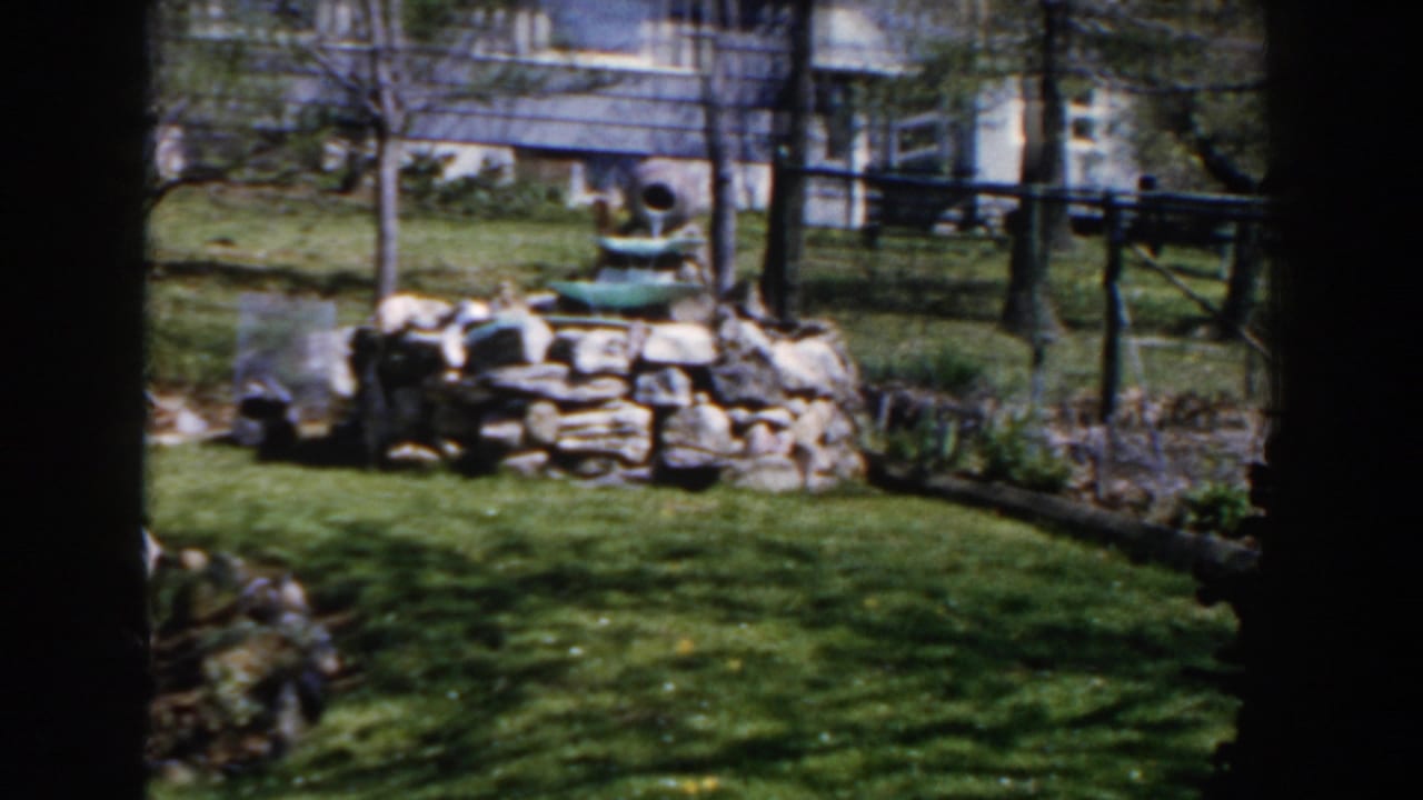 Similar backyard view with a stone fountain, lawn, trees, and residential building behind it.
