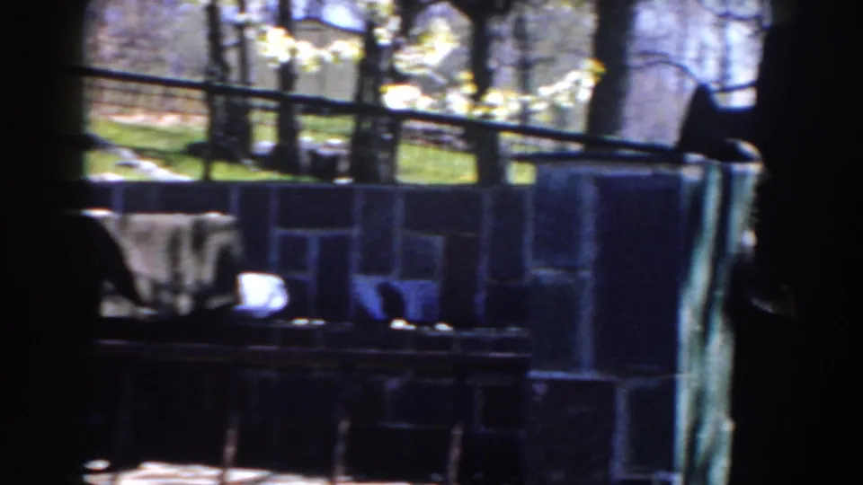 1959 Michigan 8mm frame showing a stone-walled outdoor patio area with trees, railings, a covered table, and chairs.