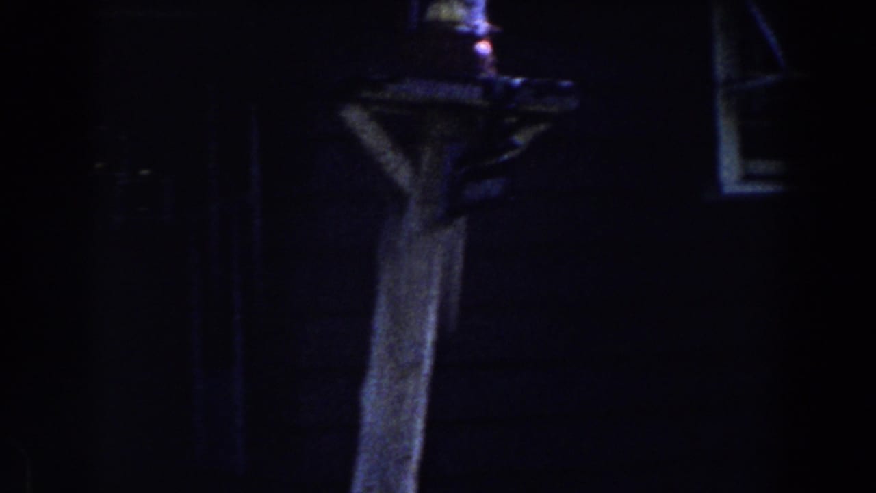 Dark house exterior with a wooden post and lantern beside a small window.