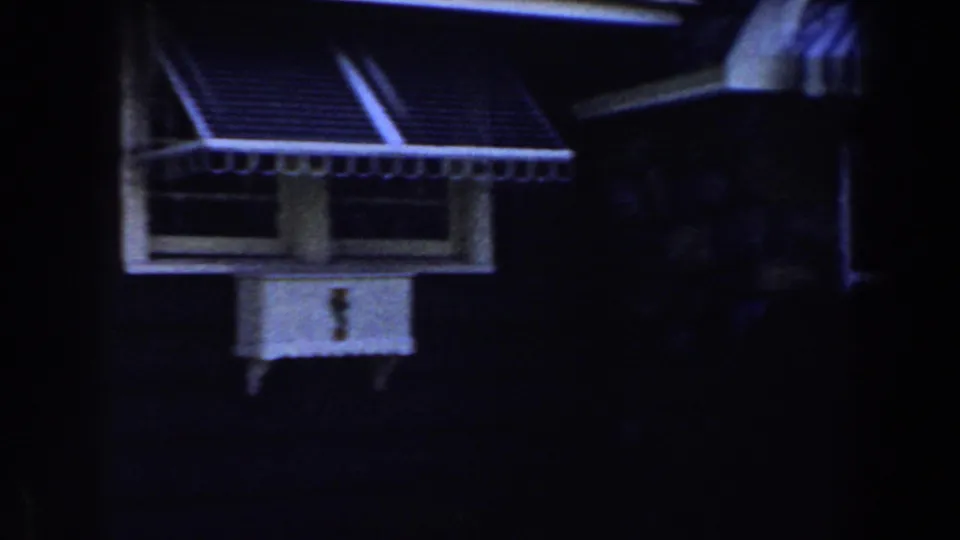 1959 Michigan home-movie frame of a small exterior window under a striped awning, seen in deep blue nighttime exposure.