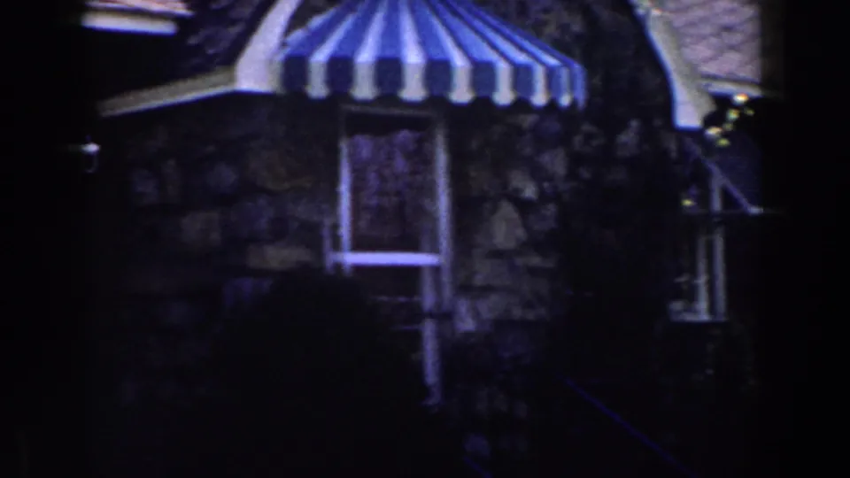 1959 Michigan 8mm frame showing a stone house exterior with a striped canopy over a doorway and a small adjacent window.