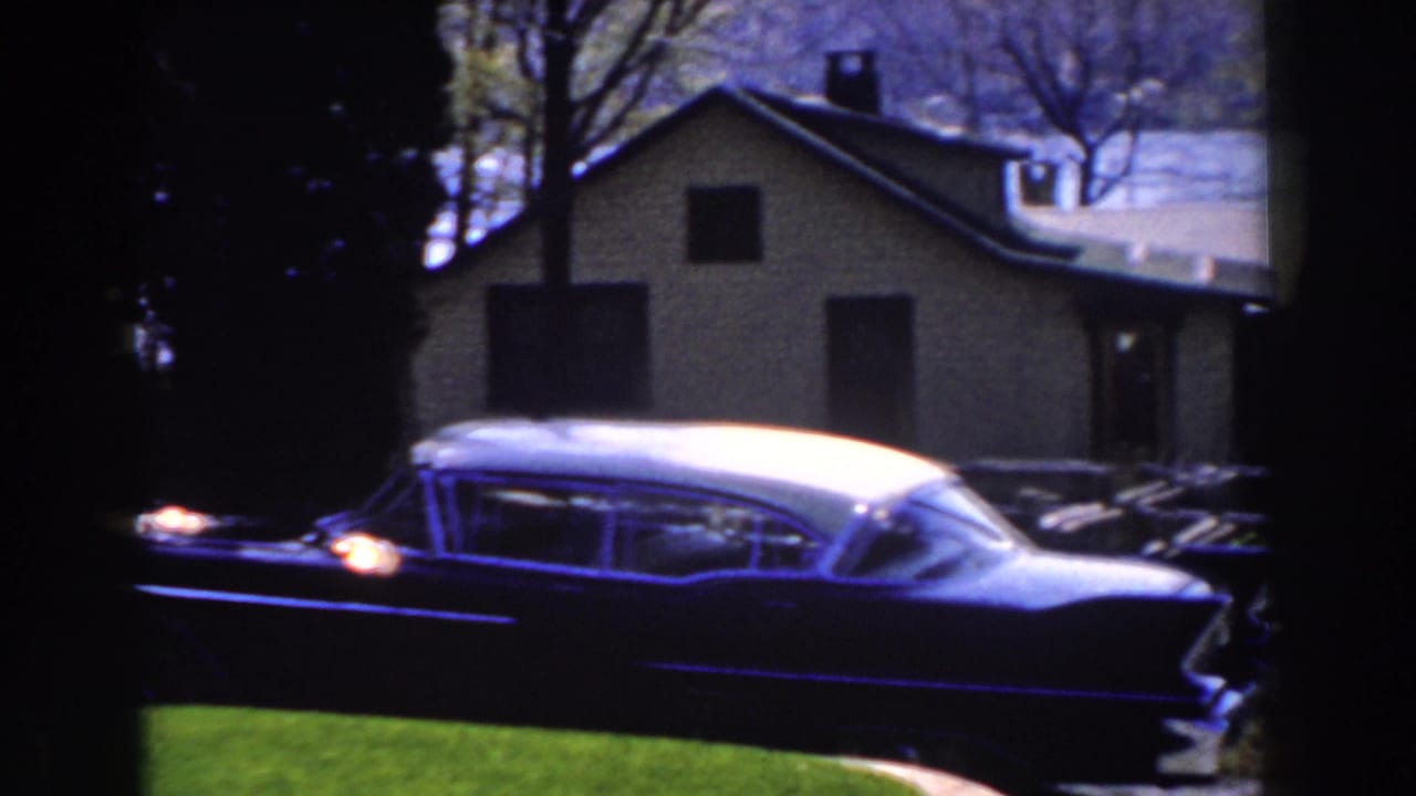 Two-tone finned car parked on grass and driveway near a house.