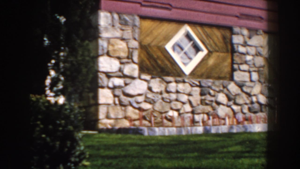 Rustic stone and wood building wall with a white diamond-shaped window above a green lawn.