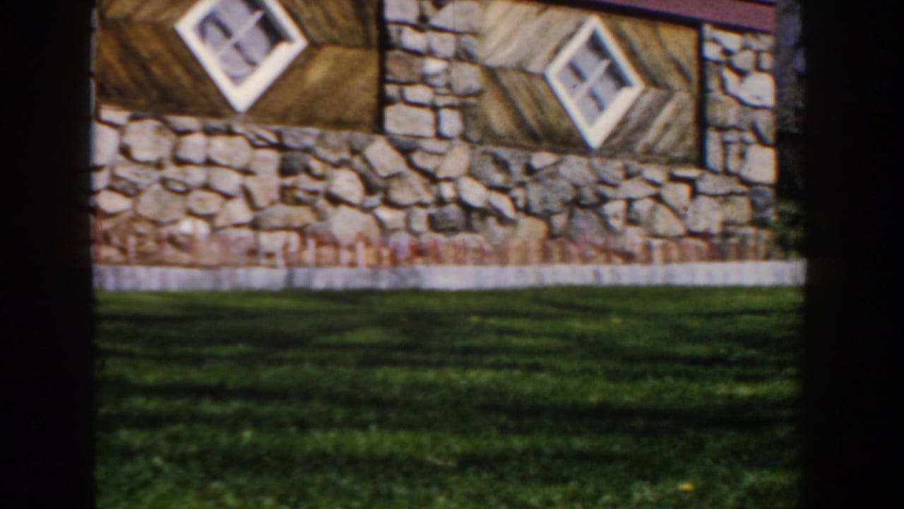 Stone building exterior with two diamond windows, wood panels, and a strip of lawn.