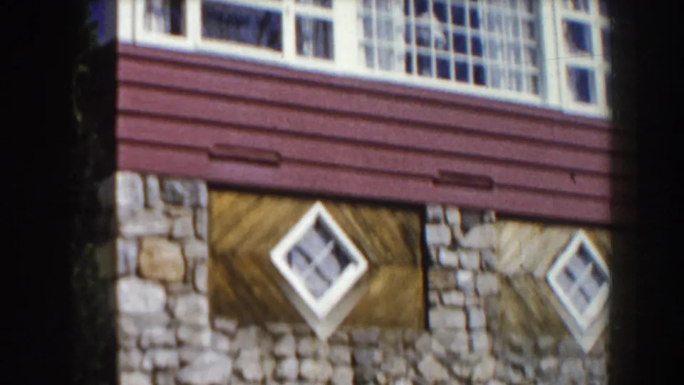 8mm frame of a red-and-white Michigan house exterior with a stone base, siding, and diamond-shaped windows.