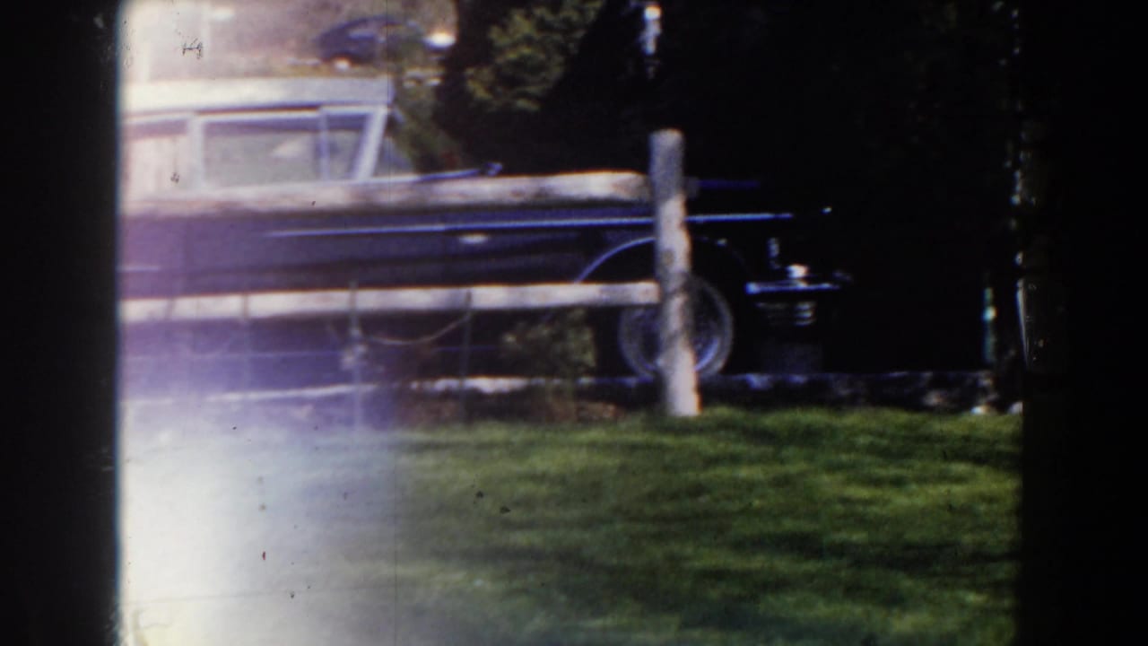 Blue sedan partly obscured by dark frame edges and a white fence.