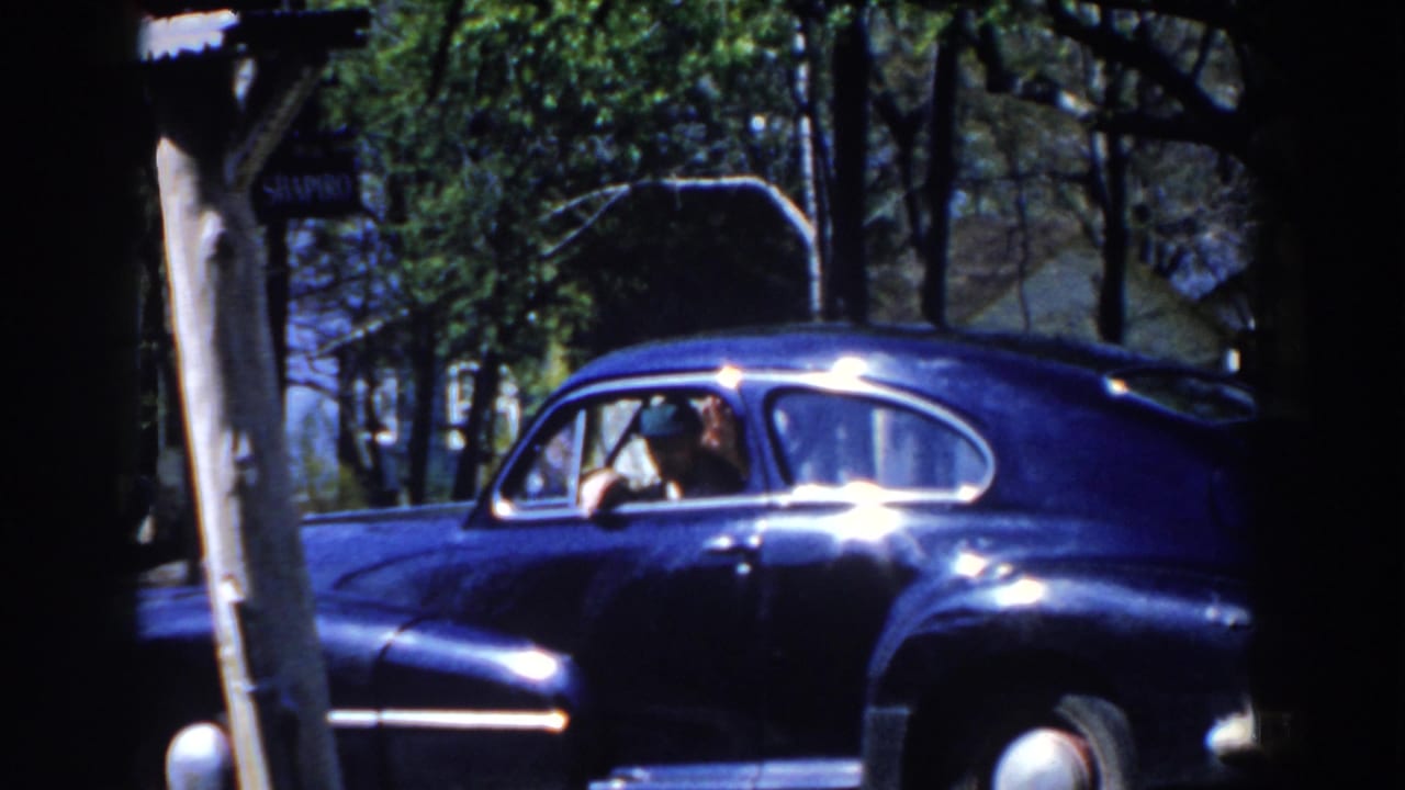 1959 Michigan frame with a blue sedan near trees and an occupant appearing to wave from the side window.