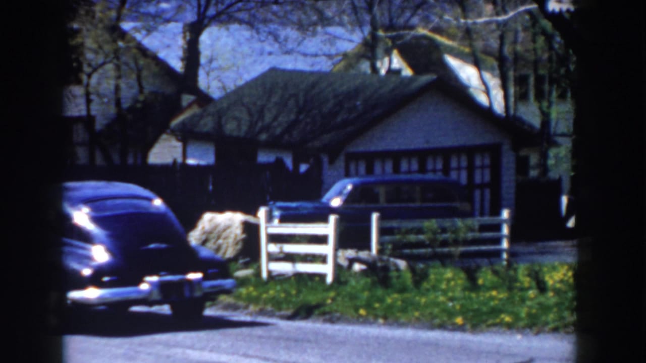 Rear of a black sedan near a white fence, house, lawn, and trees.